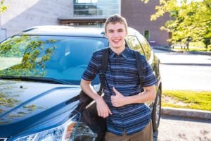 Teenage boy smiling and standing next to car