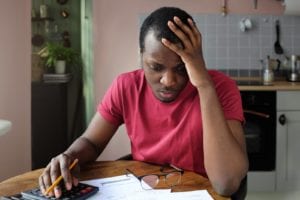An anxious man with a pencil and calculator is looking at his bills