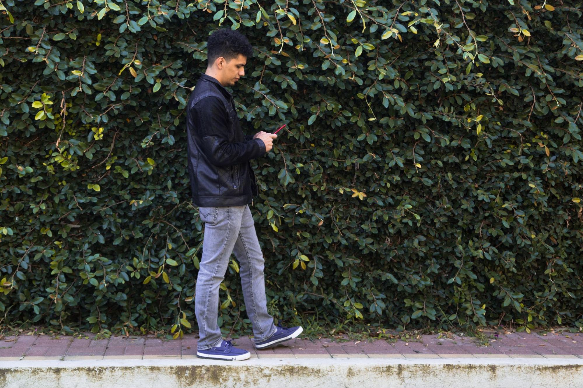 Man looking at his phone while walking on the sidewalk
