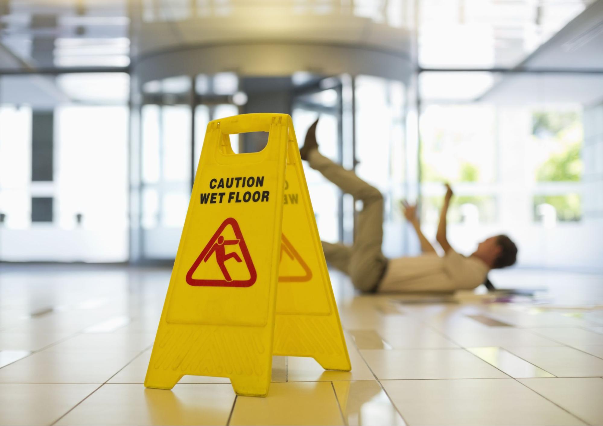 Yellow caution sign and a man slipping on wet floor in the background