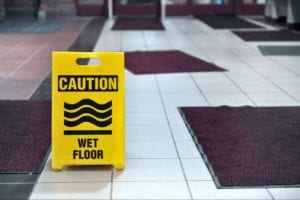 Yellow caution sign surrounded by mats on top of a wet floor